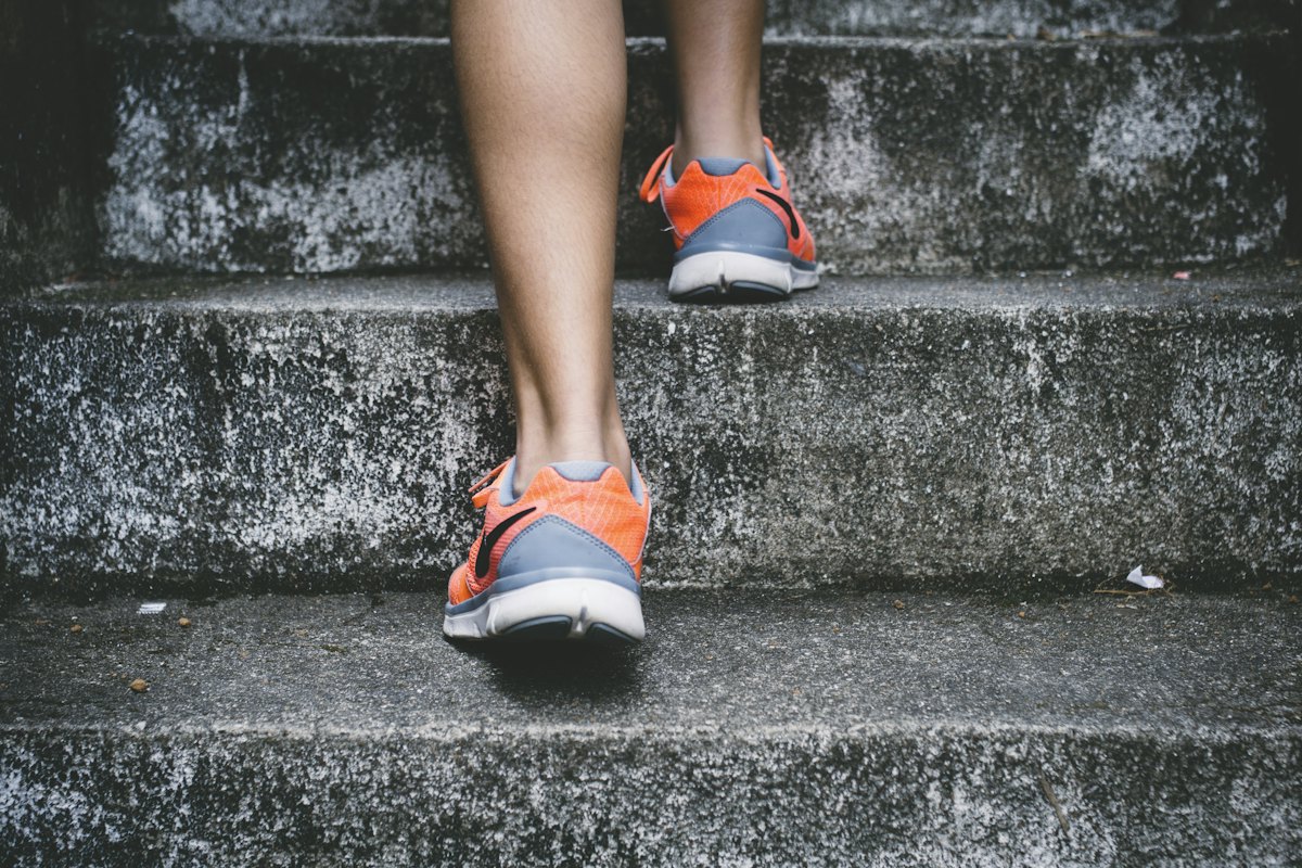 Pés com tênis de corrida subindo uma escada de concreto